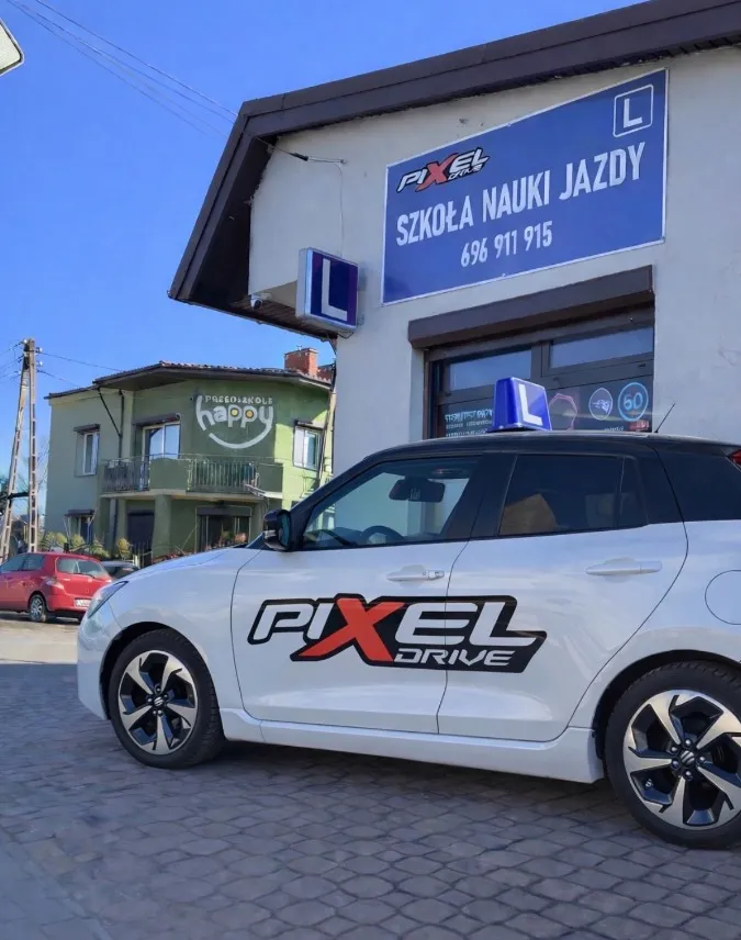Suzuki Swift PIXEL Drive przed szyldem szkoły nauki jazdy
