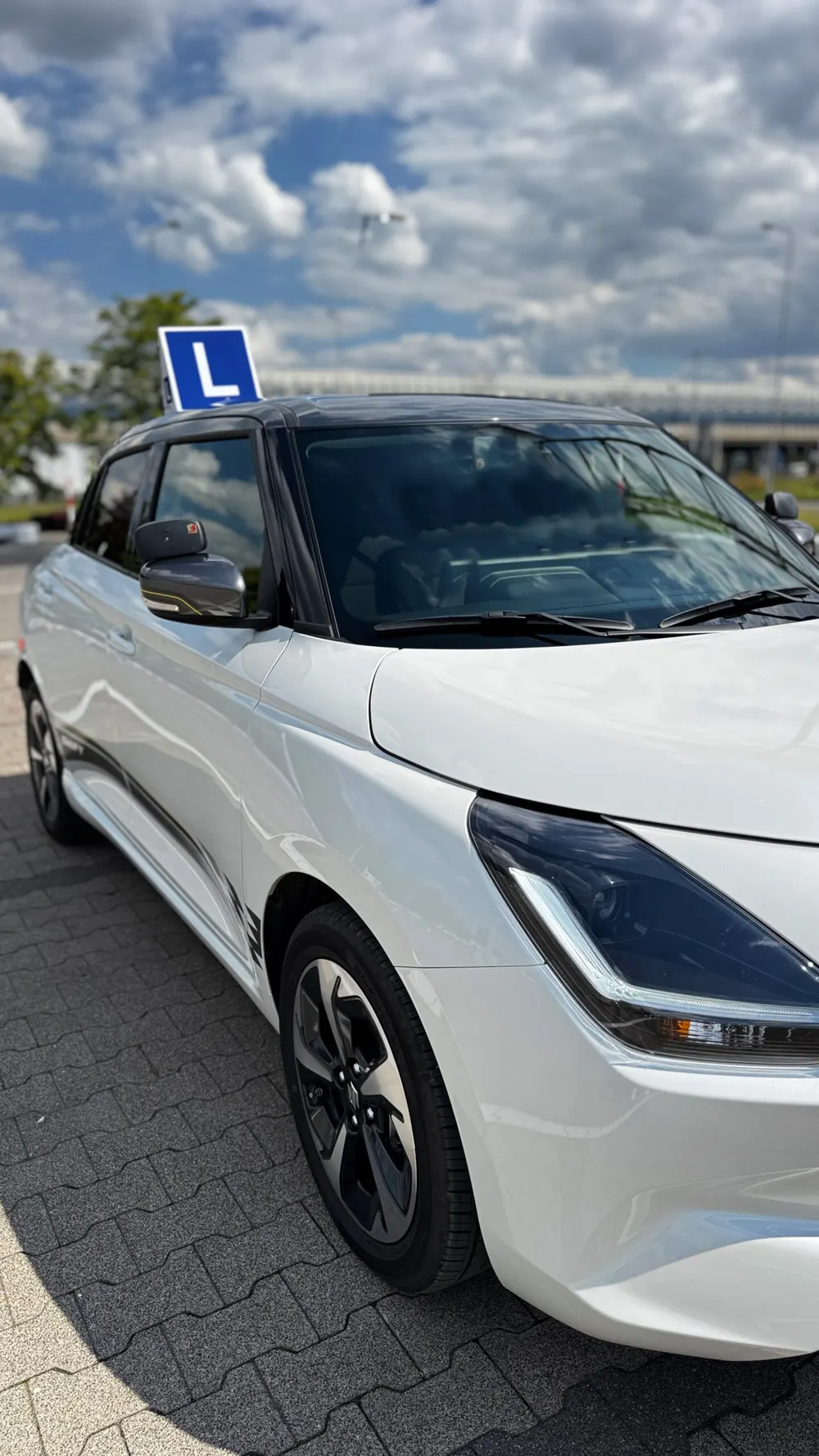 Przód Suzuki Swift z tablicą L na tle nieba